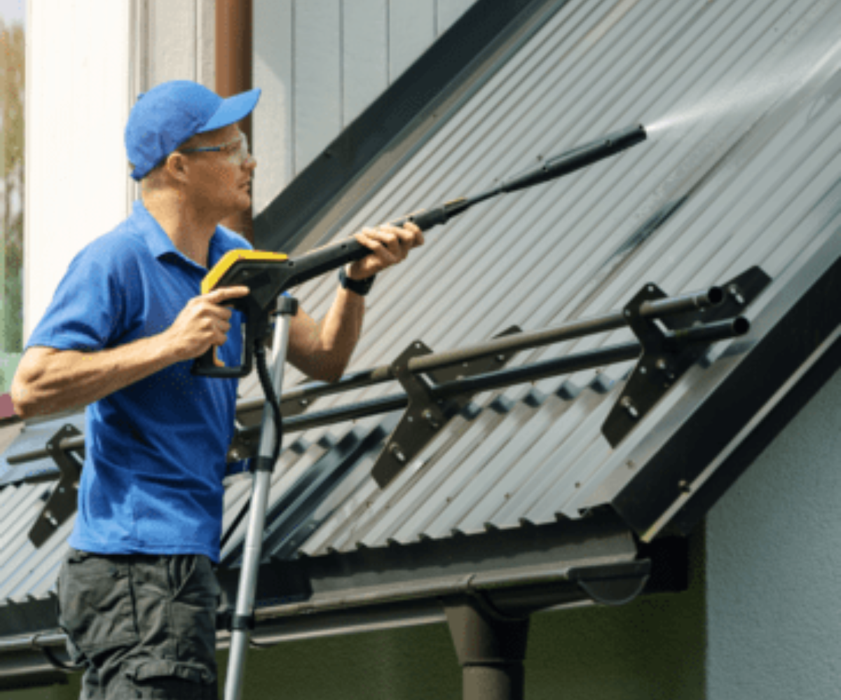 A man wearing a blue hat, blue shirt in a ladder is cleaning the gutter